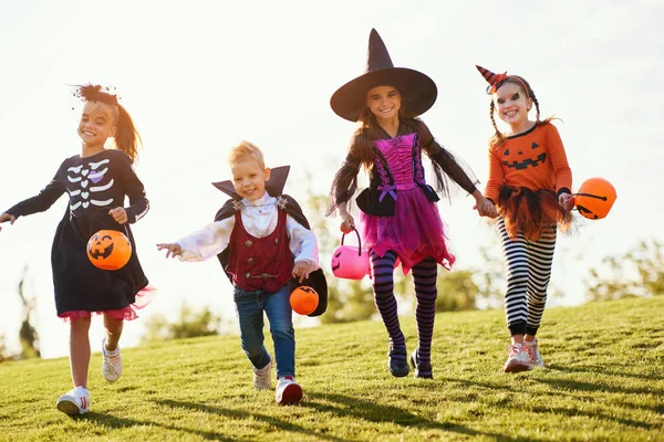 ハロウィーンの夜のお祝いの間に芝生の上で笑顔で走っている不気味な衣装を着た興奮した子供たちのグループ — ストック写真
