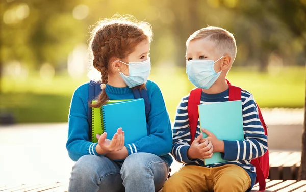 Fröhliche Kleine Jungen Und Mädchen Schutzmasken Mit Schulutensilien Plaudern Während — Stockfoto