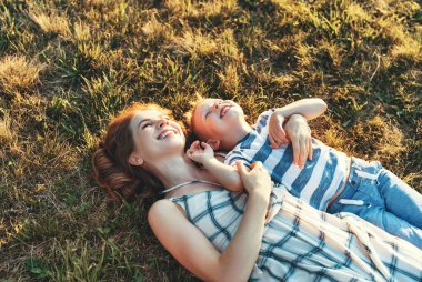 Mutlu aile: anne ve çocuk kahkahalar atıyorlar doğadaki çimlerin üzerinde.