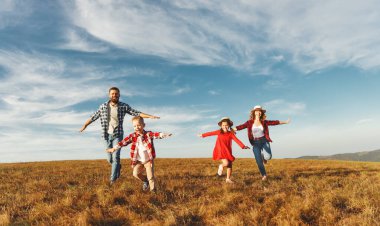 Mutlu aile: anne, baba, çocuk, oğul ve kız güneşin altında koşuyorlar.