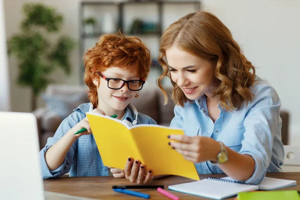 年轻妈妈帮小儿子在眼镜上做作业 一边看着儿子的笔记本 一边在网上学习 — 图库照片