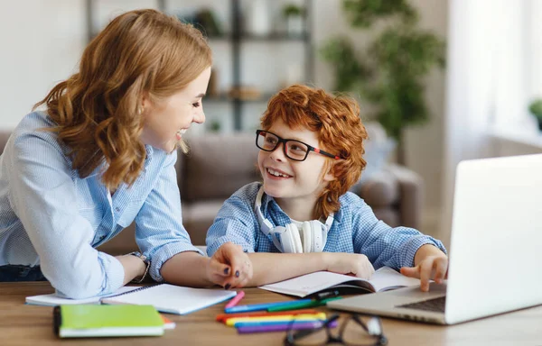 Genç anne, internette çalışırken gözlüklü oğluna ders verirken dizüstü bilgisayarı işaret ediyor.