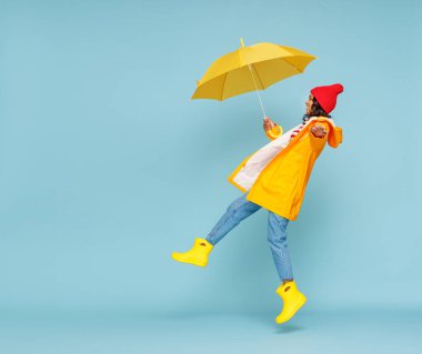 Dış giyimli, şemsiyeli, yağmurlu bir sonbahar gününde yağmurlu bir grupta hoplayıp zıplayan mutlu bir etnik kadın.