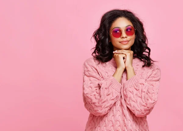 身穿针织毛衣 戴着时髦太阳镜 面带微笑地面对粉红背衬的年轻女性 — 图库照片