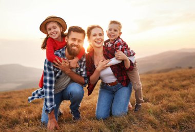 Mutlu aile: anne, baba, çocuk, oğul ve kız kucaklaşıyor, gülüyor ve çimenlerde eğleniyor, gülüyor ve güneş doğasında oynuyor.