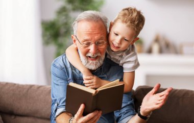 Happy family elderly  man and little boy smiling r while sitting on couch and reading fascinating fairy tale together at hom clipart