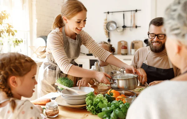 小さな娘 夫と祖母が台所のテーブルの周りに集まり 家庭での昼食のための新鮮な食材を使ったおいしい健康的な料理を準備している積極的な若い主婦 — ストック写真