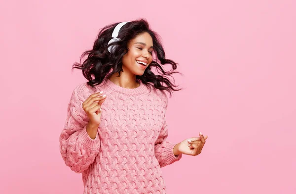 ヘッドフォンで楽観的な若い民族の女性の笑顔と指をスナップしながら 音楽を聴き ピンクの背景を背景に目を閉じて踊る — ストック写真