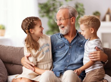 Mutlu aile küçük çocukları büyükbabalarına sarılıyor ve birlikte kanepede otururken gülüyorlar.