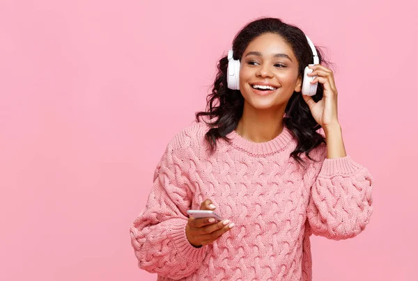 快乐的年轻女性一边在智能手机上笑着浏览社交媒体 一边听着粉色背景音乐 — 图库照片