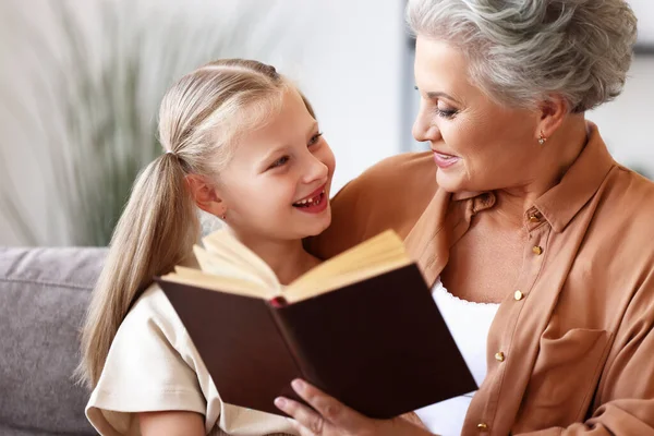 Feliz Anciana Niña Sonriendo Mirándose Mientras Están Sentadas Sofá Leyendo — Foto de Stock