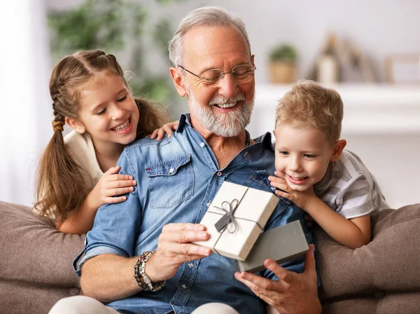 Happy family aged grandfather and grandchildren girl   and boy opening gift box while resting on sofa during holiday celebration at home