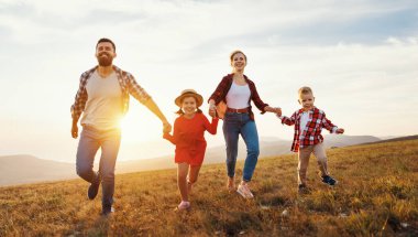 Mutlu aile: anne, baba, çocuk, oğul ve kız güneşin altında koşuyorlar.