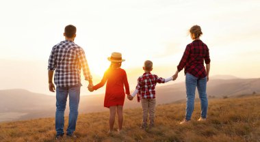 Mutlu aile: anne baba, çocuklar, oğul ve kız sırtı güneşte doğaya dönük dururlar.