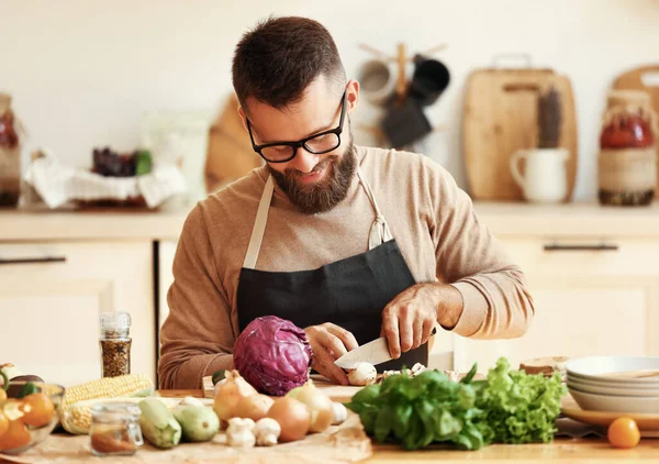 在家里的厨房里 年轻快乐的大胡子男子在木制切菜板上切围裙 准备健康的食物 配以新鲜的配料 — 图库照片