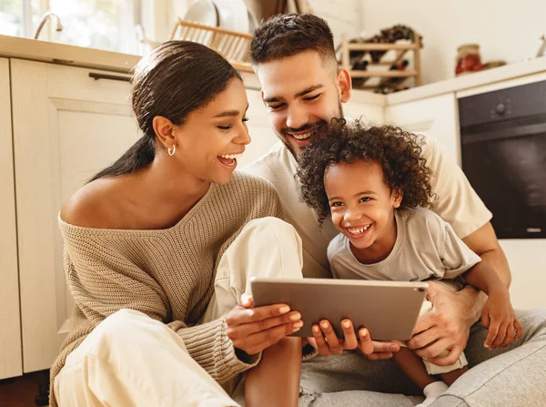 快乐的多民族家庭 父母和小儿子坐在厨房地板上 一边笑一边看平板电脑上有趣的视频 — 图库照片