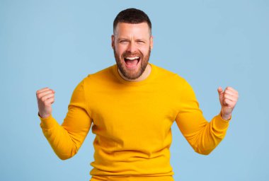 Sarı kazaklı mutlu anlamlı adam zaferi ve zaferi kutluyor.