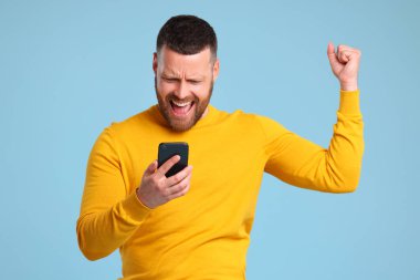 Sarı kazaklı, mutlu, etkileyici adam mavi bir grupta zafer ve zaferi kutluyor.