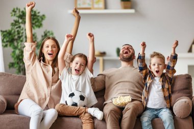 Hayranlardan oluşan bir aile. Anne, baba ve çocuklar futbol maçı izleyip evdeki golü kutluyorlar.