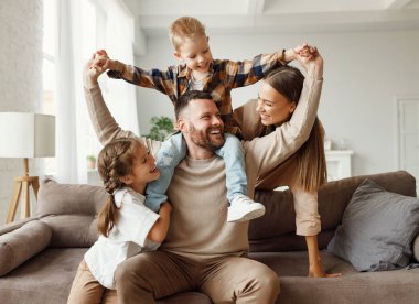 Mutlu aile anne baba ve çocuklar evde kanepede oynar ve gülerler. 