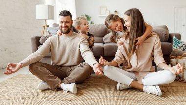 Mutlu aile: Çocuklar evde eğlenirken ve sarılırken huzurlu, genç ebeveynler Lotus pozisyonunda oturup meditasyon yapıyorlar.