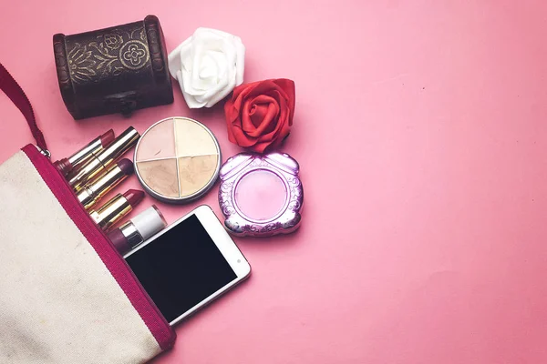 化妆袋包含了丰富多彩的口红和脸粉和电话 珠宝盒 红色和白色的花朵在粉红色的背景 — 图库照片