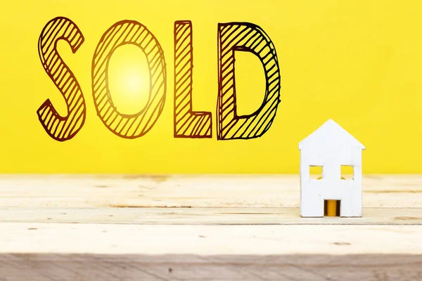 sold home, sold text and small white wood house on table with yellow backdrop