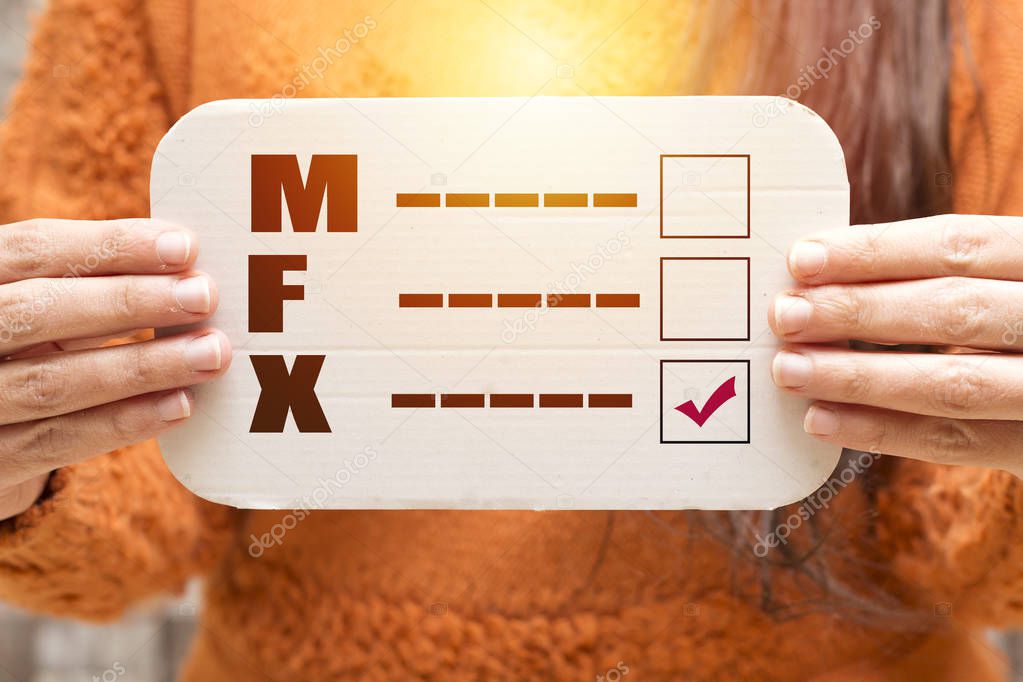 closeup of a young caucasian person holding a form with the letters M for male, F for female and X for the third gender category, written in it, with a check mark on the X