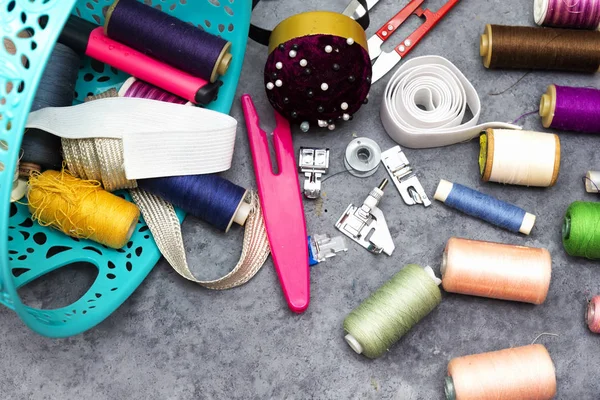 basket of sewing tools :  scissors, colorful  bobbins with thread and presser foot on gray  wooden table