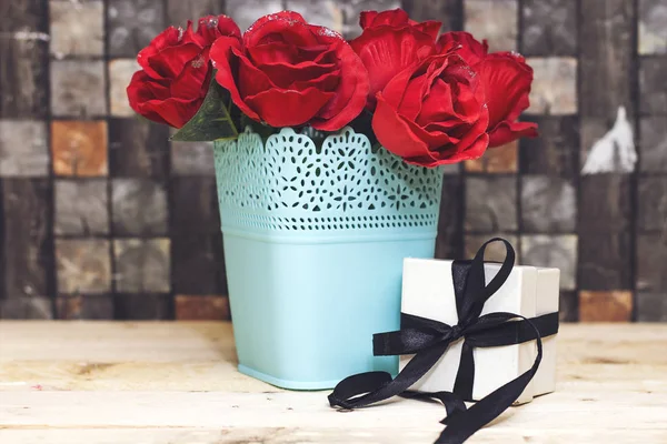 white small box present with black ribbon  and roses flowers in plastic vase on wood table for holiday