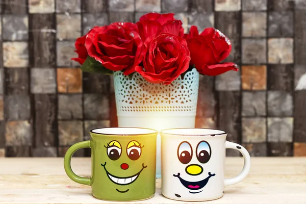 Two coffee cup with smiling face of man and woman together with roses vase. Concept of happy Valentines day