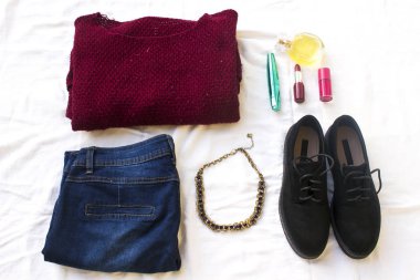 Mavi jeans, kırmızı büyük boy örme kazak ve siyah düz ayakkabı, kolye ve pembe oje, maskara, şişe parfüm beyaz sayfa üzerinde. Kadının rahat gün kıyafetler havai görünümü. Trendy hipster bak.