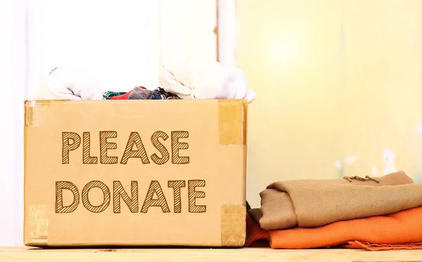 clothes in carton box on wood table for donation, coat drive concept, please donate text