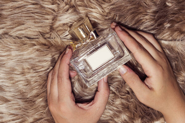 женщина держит бутылку духов на меховой ткани
