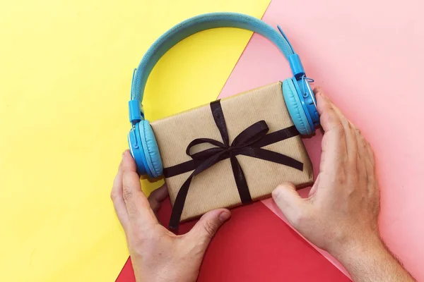 Christmas music gift concept. hand man holding headphones and gift boxes on colorful background