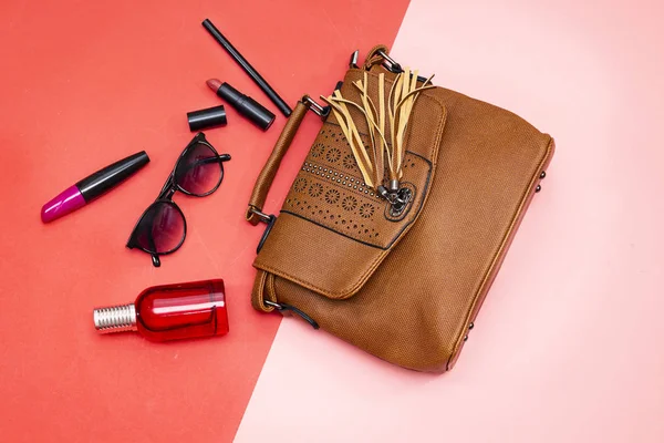   Ruj ve rimel fırçası, şişe parfümü güneş gözlüğü ve göz kalemi ve pembe ve kırmızı kağıtta omuz çantası.