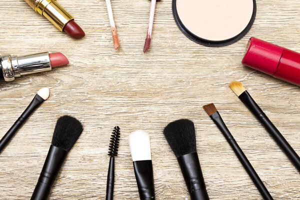 foundation powder, variety lipstick and lip gloss, brush and nail polish on wood table