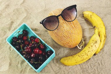 kum üzerinde güneş gözlüğü, muz ve kiraz sepeti giyen kavun 