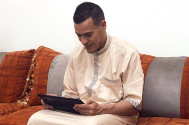 Müslüman adam koltukta Faslı olarak oturuyor ve tablet kullanarak çalışıyor.