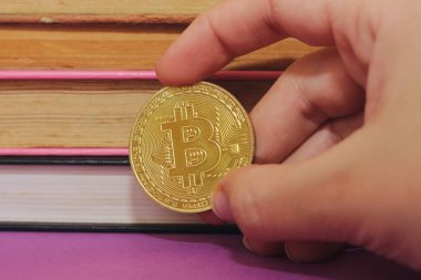 kitap arka plan ile bir bitcoin tutan closeup el