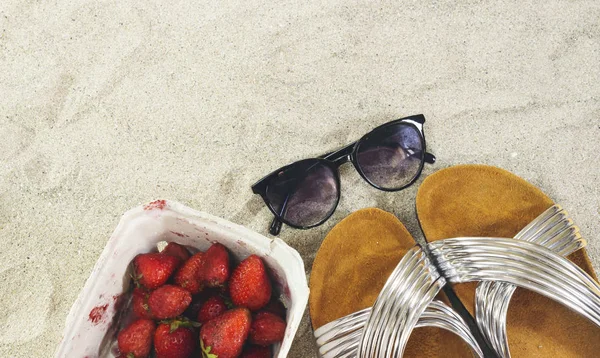Sunglasses and slippers and strawberry box on sand, summer concept