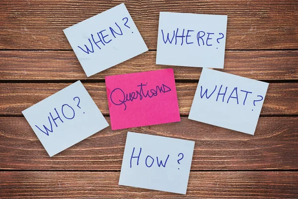 Questions - Why? What? Where? When? Why? How? on blue stickers on wooden background. Business, text, communication, information, message, note, paper, word