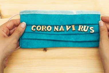 Elleri tıbbi bir maske tutuyor ve tahta alfabelerden koronavirüs oluşturuyor.