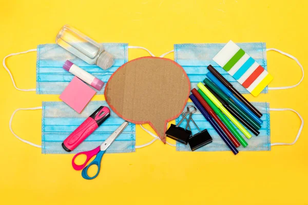 Back to school, school supplies and chat cardboard bubble on a yellow background. Protection of schoolchildren and students from the virus