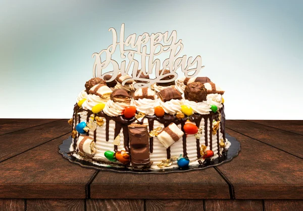 Birthday layer cake decorated with chocolate pieces with happy birthday text on wooden board