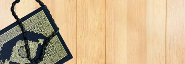 Kutsal Kur 'an' ın Arapça kaligrafi anlamı ve ahşap masada siyah tespih.