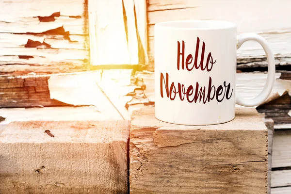İçinde Hello November yazan bir fincan kahve, ahşap küpün üstünde.
