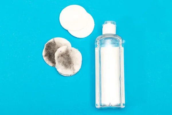 Makeup remove skin care. Tonic for face skin or makeup remover in a plastic bottle, cotton pads on blue background. Hygiene supplies, beauty tools and skin