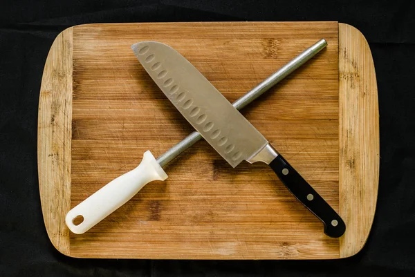Um afiador de facas, ou aço afiado, e uma faca de chef em uma tábua de corte — Fotografia de Stock