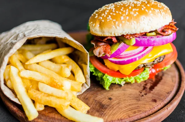 Hamburguesa y papas fritas sobre una mesa de madera sobre fondo negro — Foto de Stock